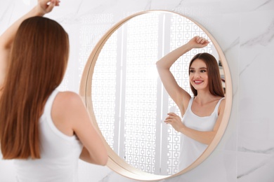 Beautiful young woman applying deodorant in bathroom