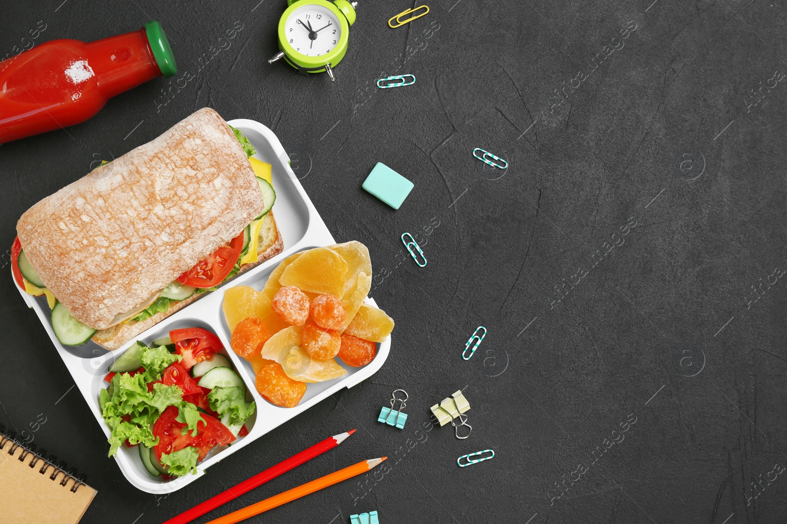 Photo of Flat lay composition with lunch box, appetizing food and stationery on dark background