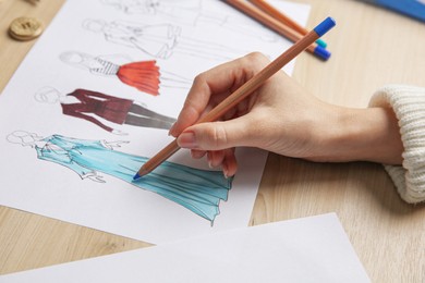 Photo of Fashion designer creating new clothes in sketchbook at wooden table, closeup