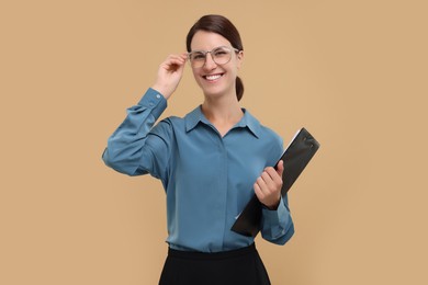 Photo of Happy secretary with clipboard on beige background