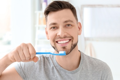 Young man brushing his teeth indoors