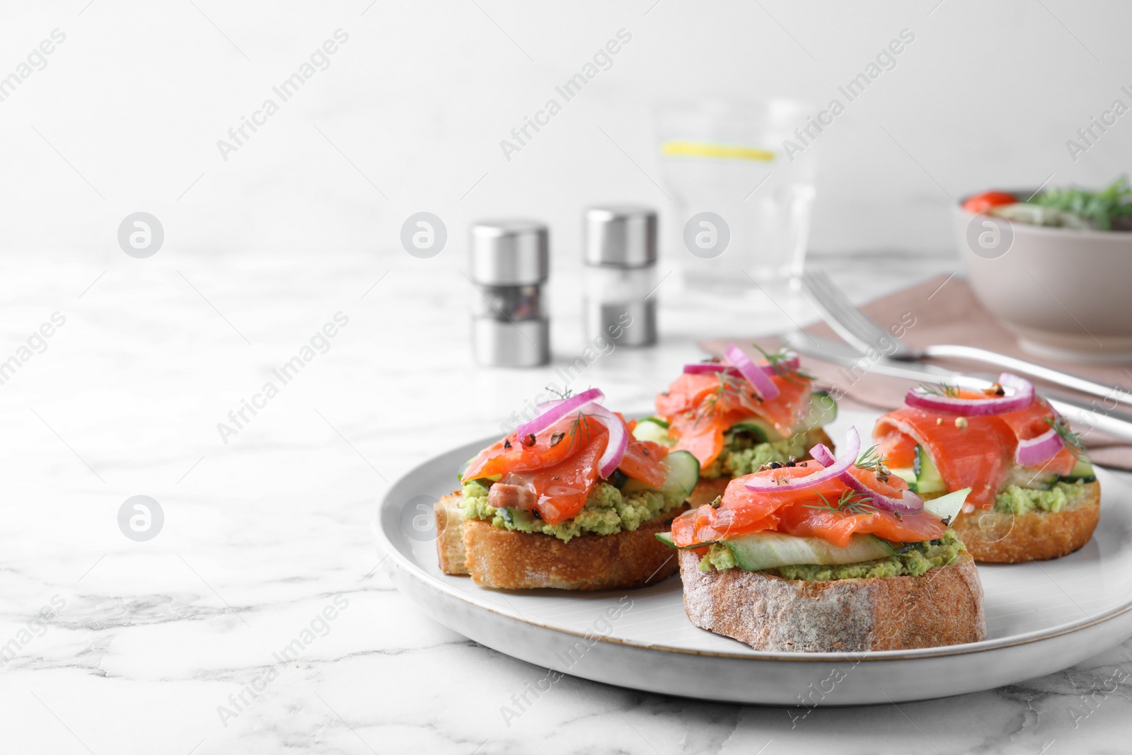 Photo of Delicious sandwiches with salmon, avocado, cucumber and onion on white marble table. Space for text