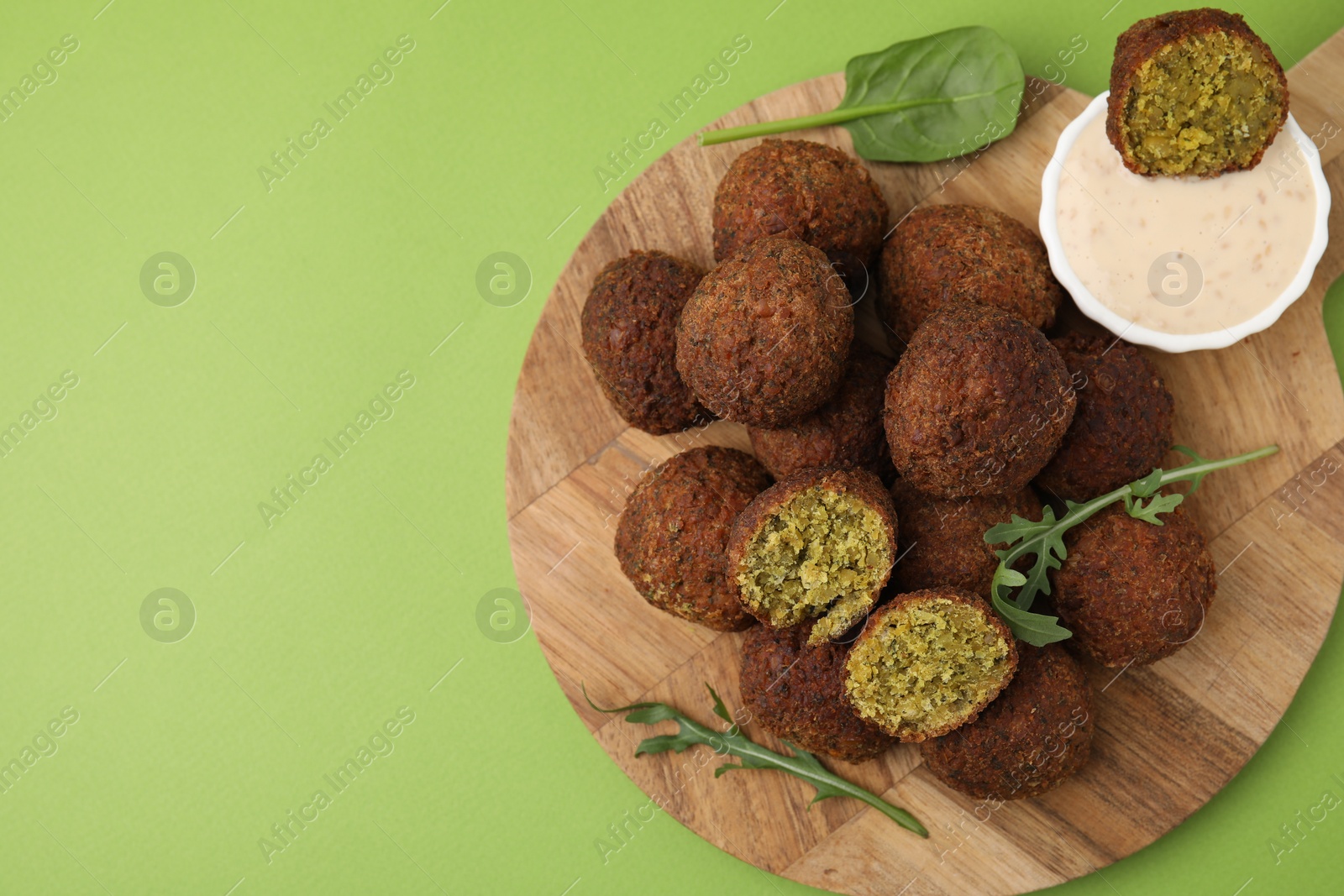 Photo of Delicious falafel balls, herbs and sauce on green background, top view. Space for text