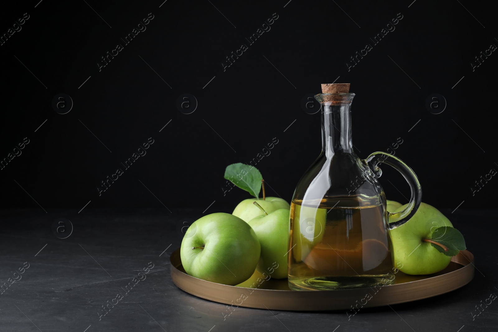 Photo of Fresh ripe green apples and jug of tasty juice on black table, space for text