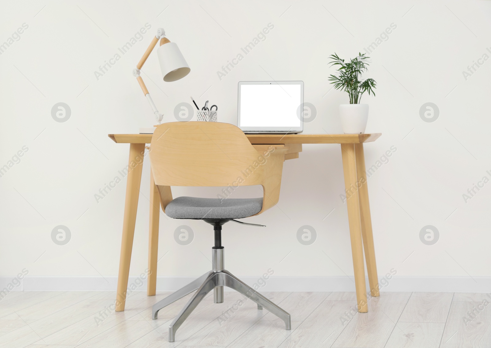 Photo of Stylish office interior with comfortable chair, desk, laptop and lamp