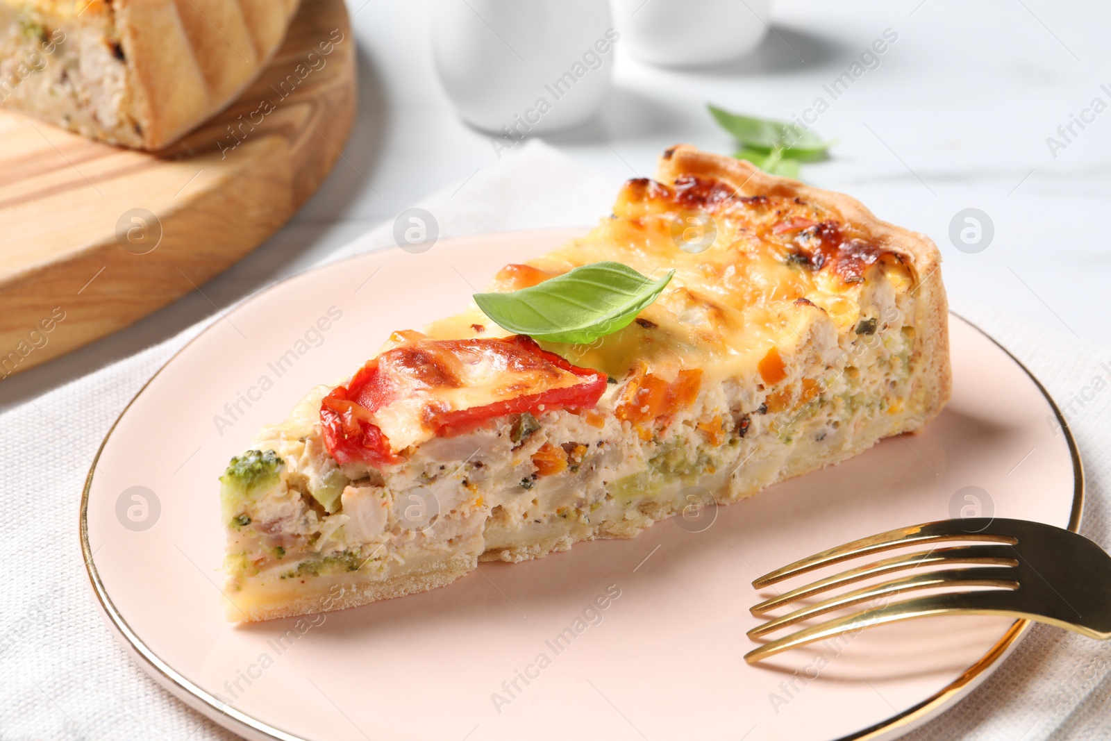 Photo of Piece of tasty quiche with chicken, cheese, basil and vegetables on white table, closeup