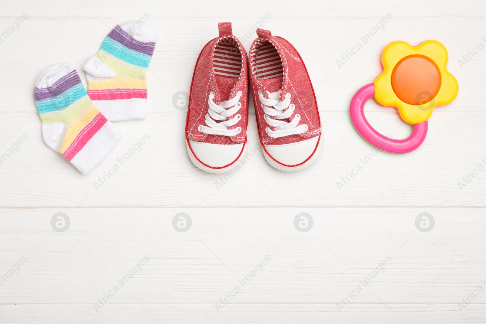 Photo of Child's booties, teether and socks on white wooden table, flat lay. Space for text