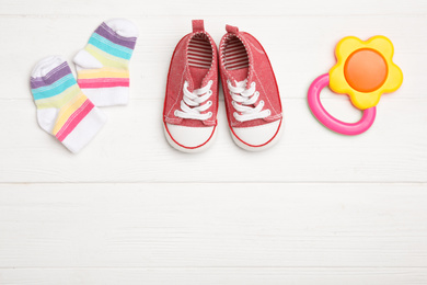 Photo of Child's booties, teether and socks on white wooden table, flat lay. Space for text