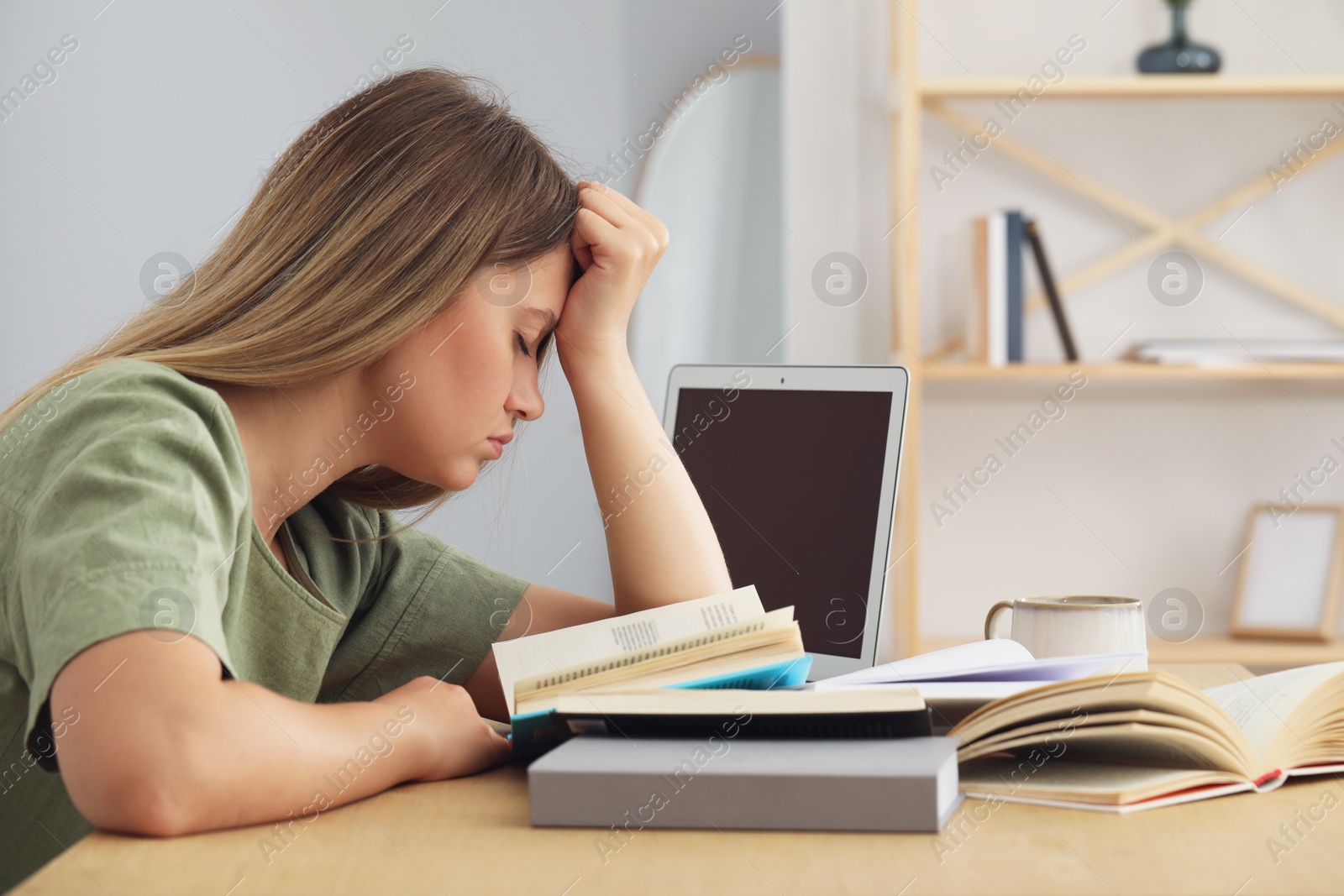 Photo of Sleepy young woman studying at wooden table indoors