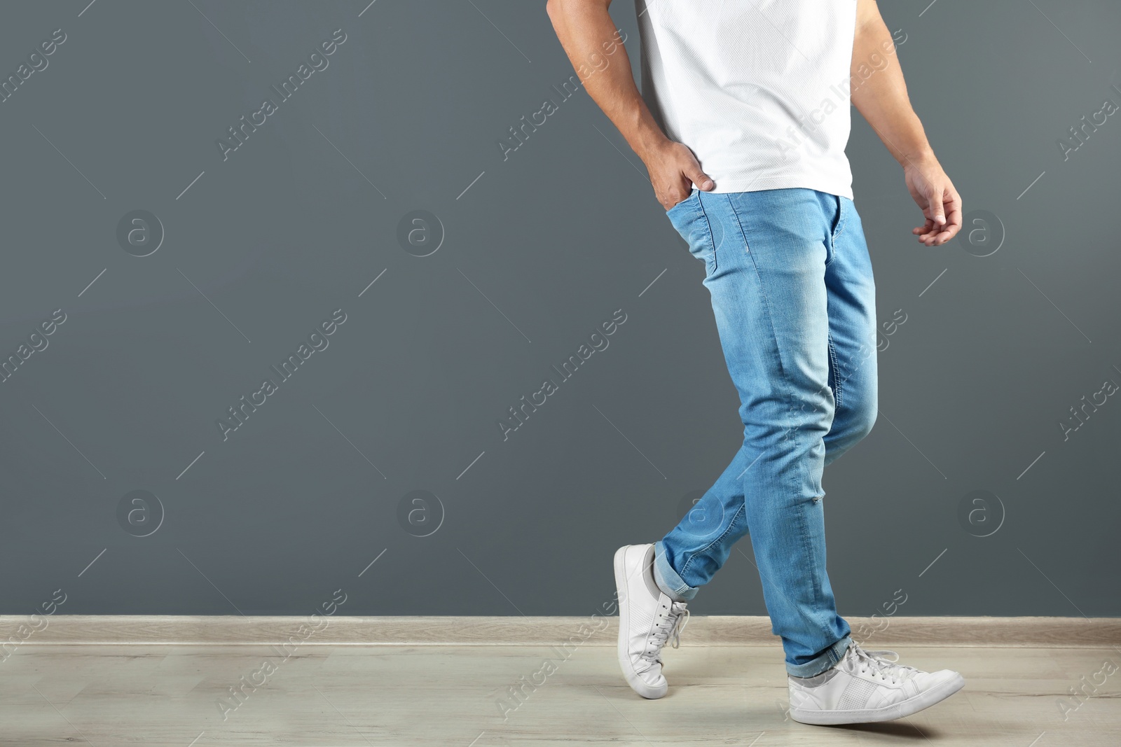 Photo of Young man in stylish jeans near grey wall with space for text, focus on legs