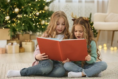 Photo of Cute little girls reading book at home. Christmas atmosphere
