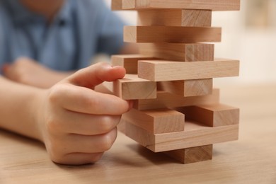 Child playing Jenga at wooden table indoors, closeup