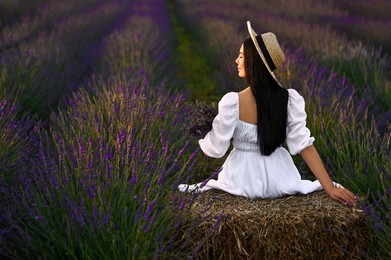 Photo of Woman sitting on hay bale in lavender field, back view
