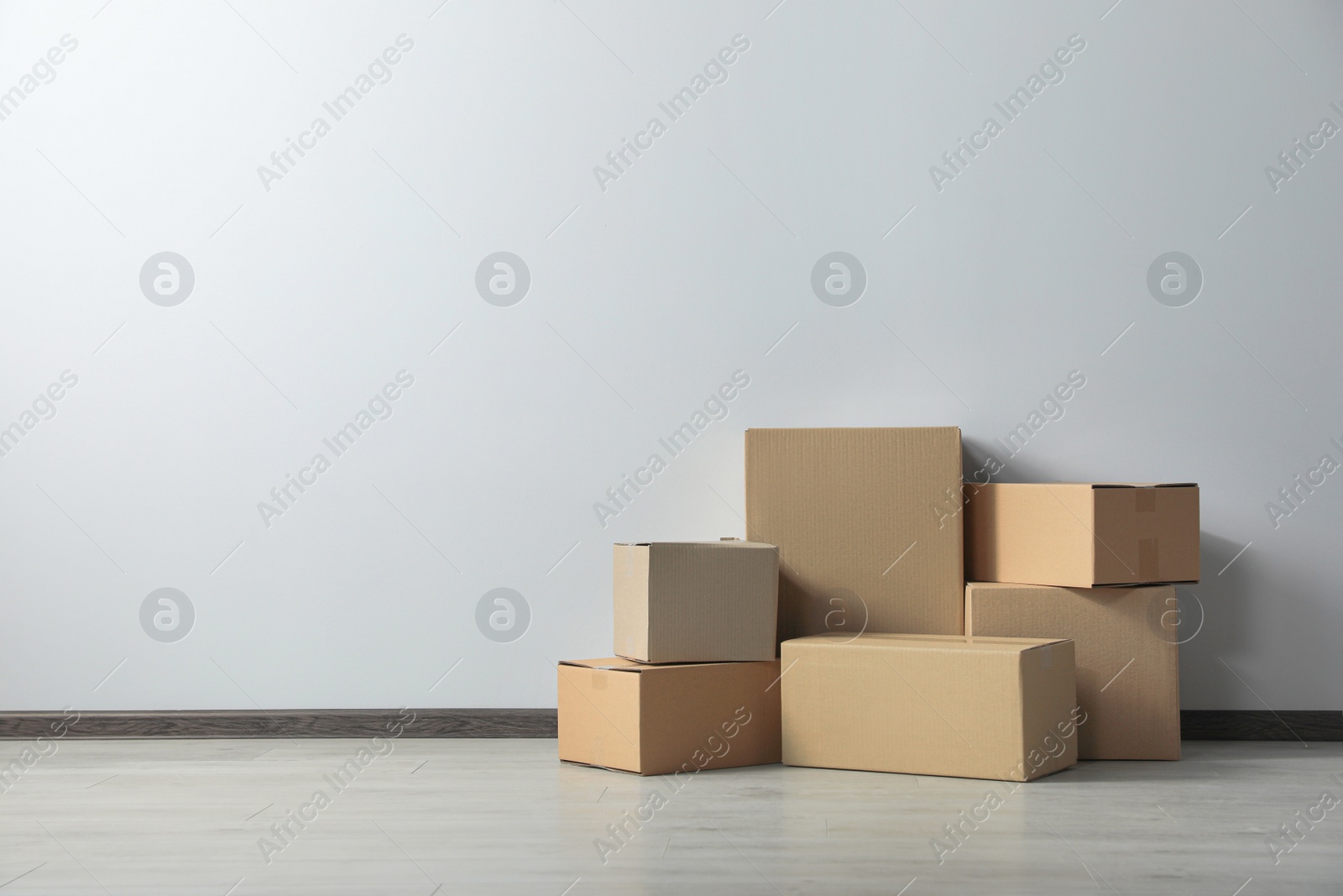 Photo of Many closed cardboard boxes on floor near white wall, space for text. Delivery service