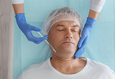 Photo of Mature man with double chin receiving injection in clinic, above view