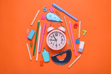 Photo of Flat lay composition with different school stationery and alarm clock on red background. Back to school