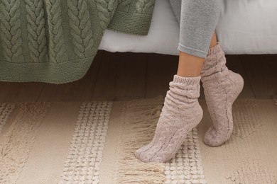 Photo of Woman wearing warm knitted socks at home, closeup. Space for text