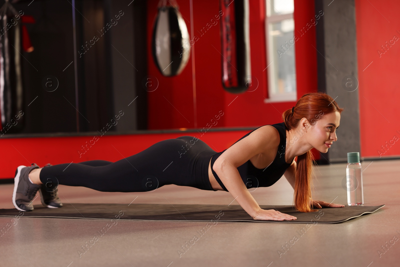 Photo of Athletic young woman doing push ups on mat in gym