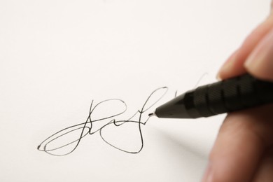 Photo of Woman writing her signature with pen on sheet of white paper, closeup