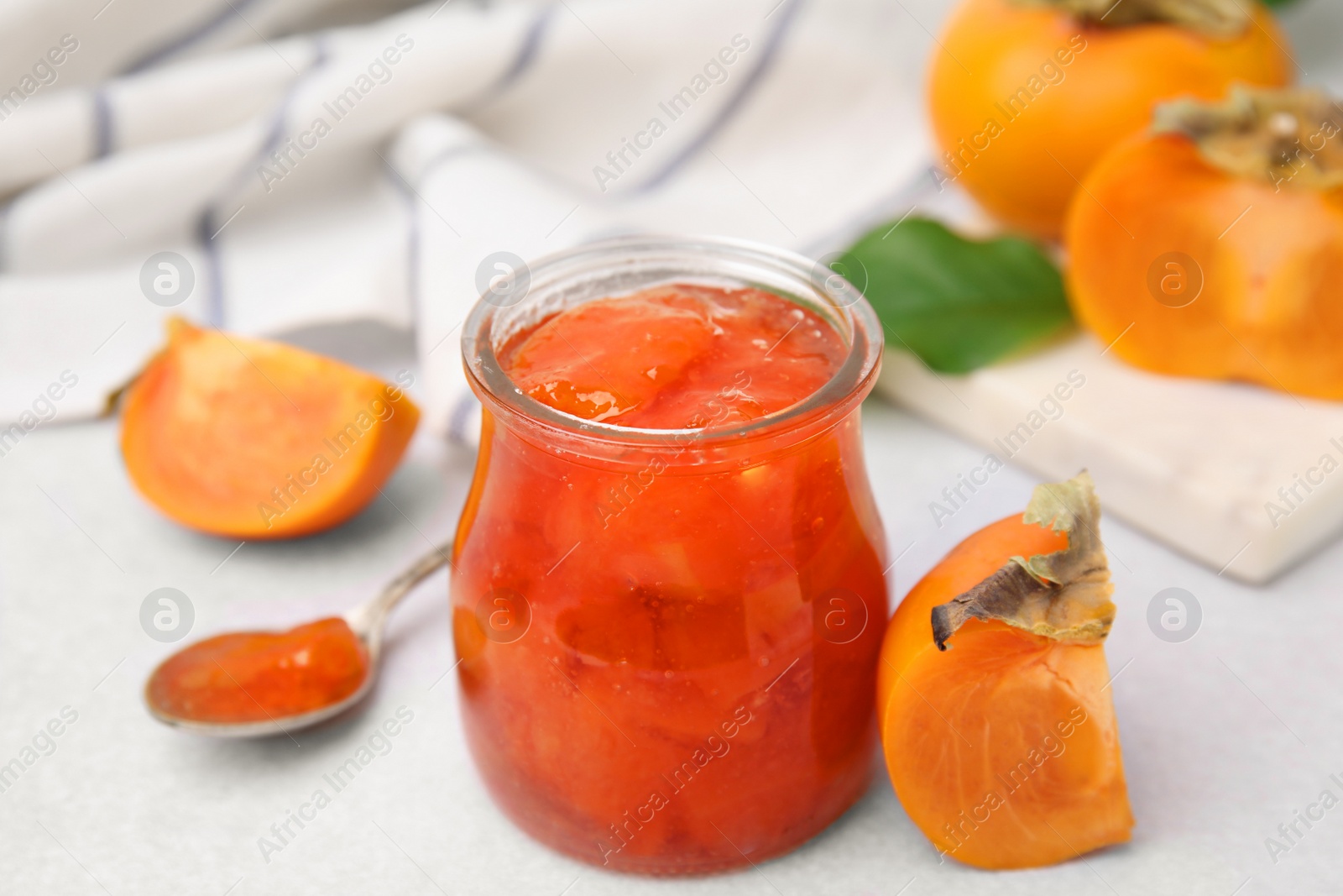 Photo of Jar of tasty persimmon jam and ingredients on white table