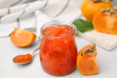 Photo of Jar of tasty persimmon jam and ingredients on white table