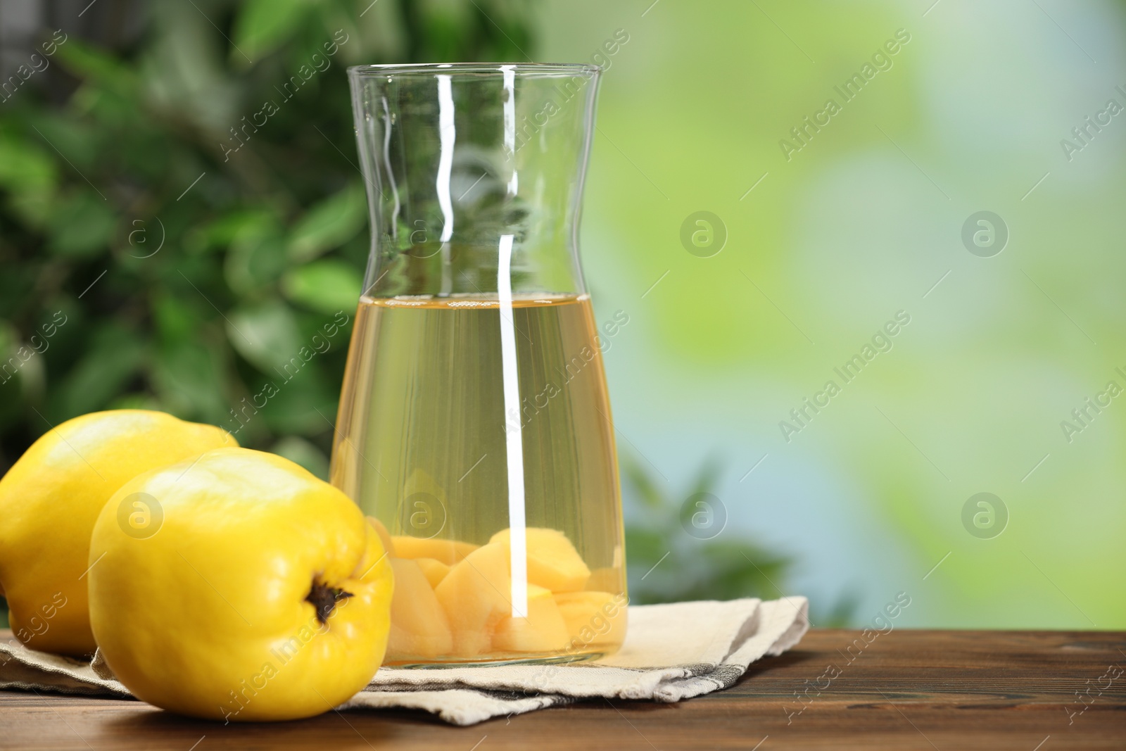 Photo of Delicious quince drink and fresh fruits on wooden table against blurred background. Space for text