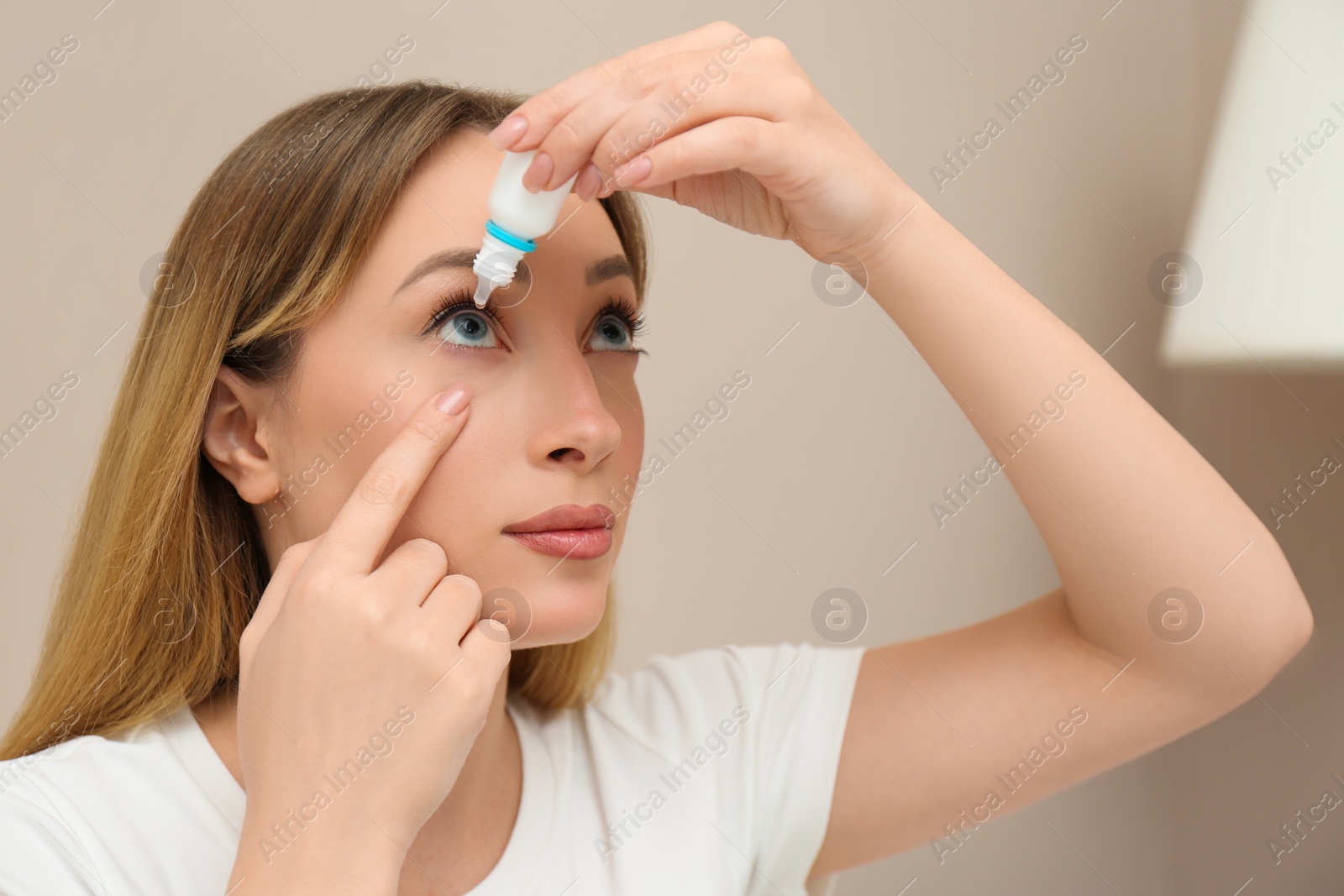 Photo of Young woman using eye drops at home