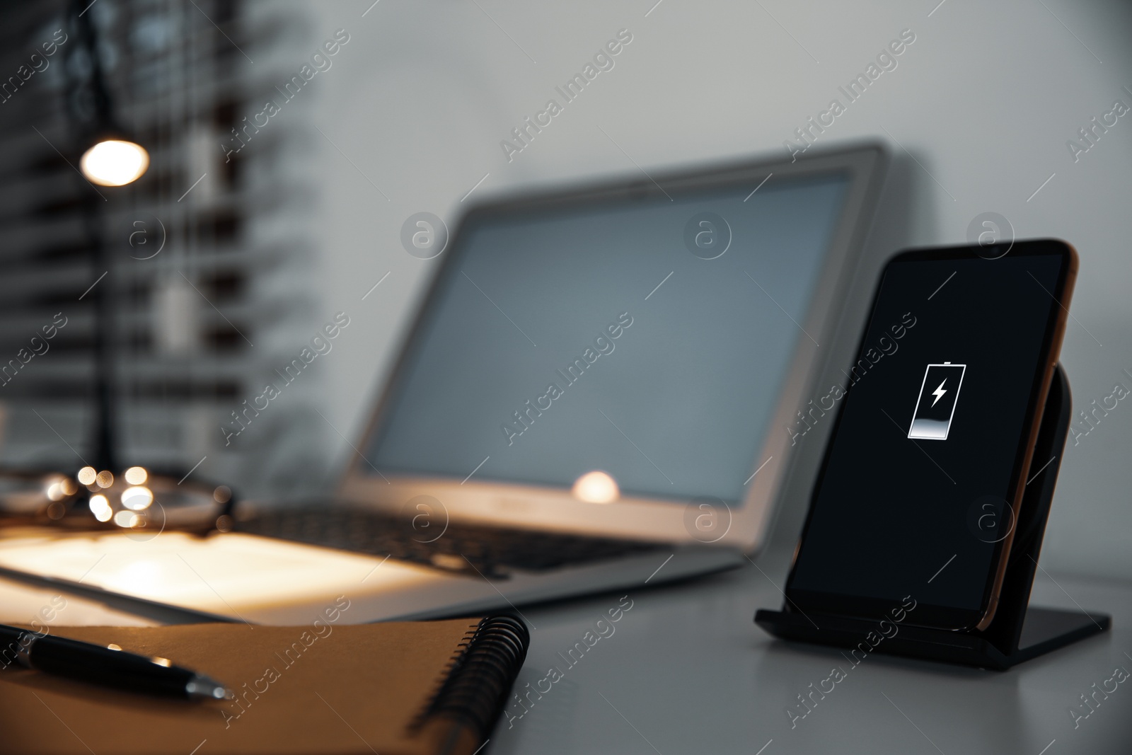 Photo of Mobile phone with wireless charger on table. Modern workplace accessory