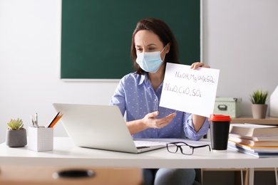 Photo of Teacher with protective mask conducting online lesson in classroom during COVID-19 quarantine