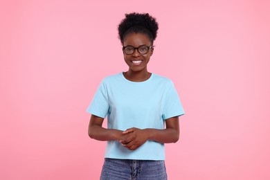 Portrait of happy young woman in eyeglasses on pink background