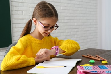 Photo of Girl with stylish smart watch at wooden table in school