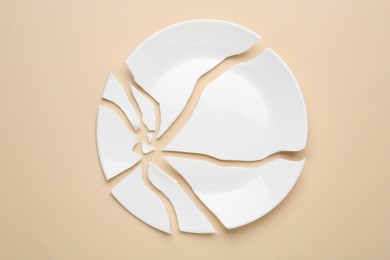 Photo of Pieces of broken ceramic plate on beige background, flat lay