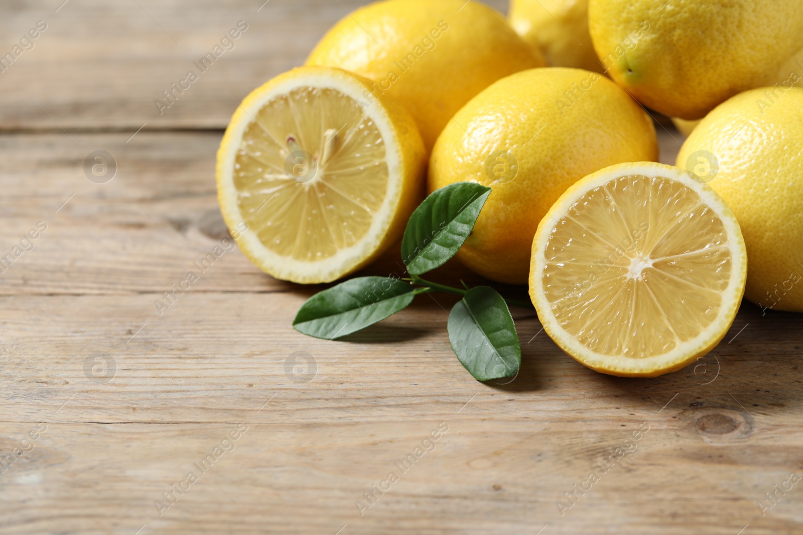 Photo of Fresh lemons and green leaves on wooden table, closeup. Space for text