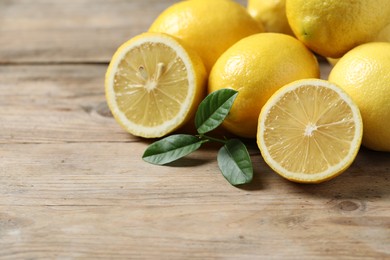 Fresh lemons and green leaves on wooden table, closeup. Space for text