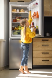 Photo of Girl taking bottle with juice out of refrigerator in kitchen