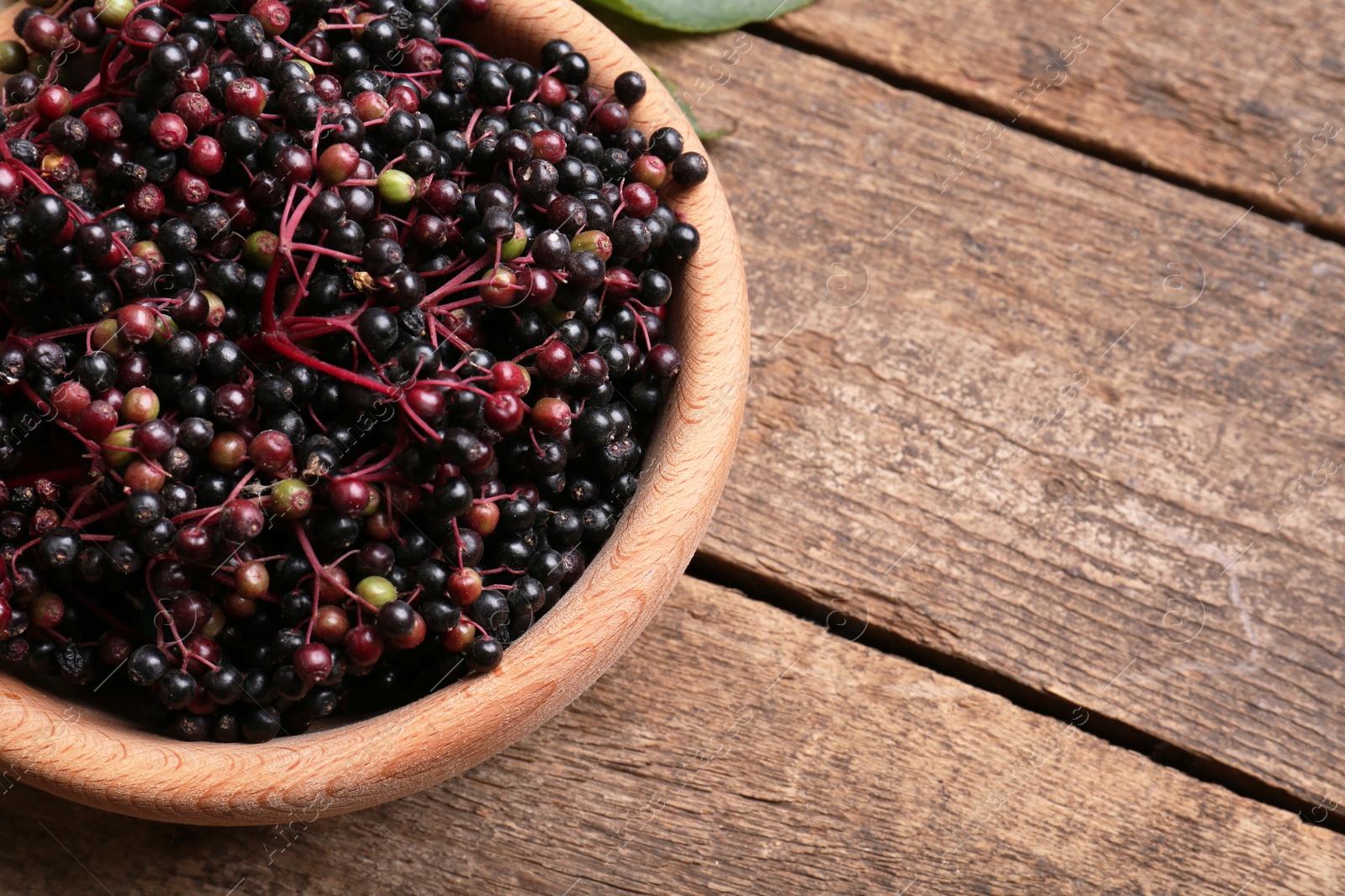 Photo of Bowl with tasty elderberries (Sambucus) on wooden table, top view. Space for text