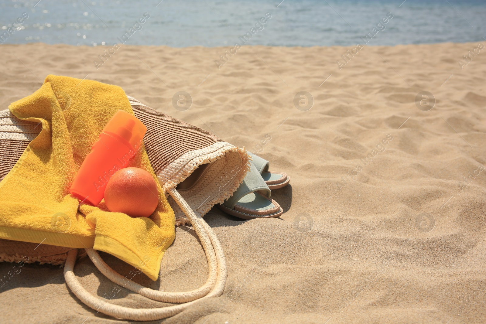 Photo of Beach bag, sunscreen and other accessories on sand near sea. Space for text
