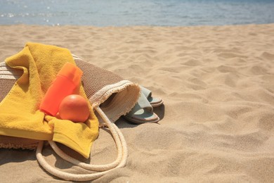 Beach bag, sunscreen and other accessories on sand near sea. Space for text