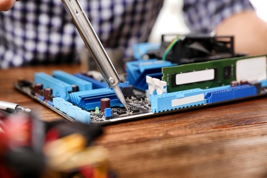 Photo of Repairing motherboard with soldering iron on table, closeup