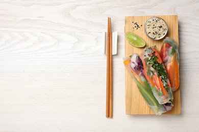 Photo of Delicious rolls wrapped in rice paper served on white wooden table, flat lay. Space for text