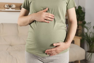 Pregnant woman touching belly in living room, closeup