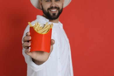 Young man with French fries against red background, focus on hand. Space for text