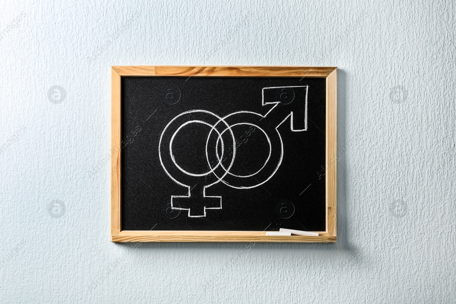 Photo of Small blackboard with drawn gender symbols on white wall. Sex education