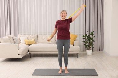 Photo of Senior woman doing exercise with fitness elastic band on mat at home
