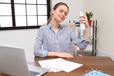 Young woman applying thermal water on face in office. Cosmetic product