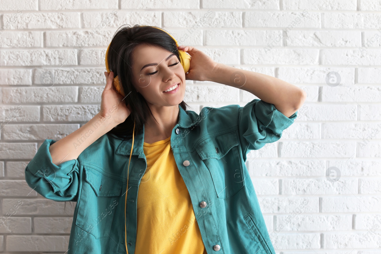 Photo of Portrait of beautiful woman listening to music with headphones near brick wall