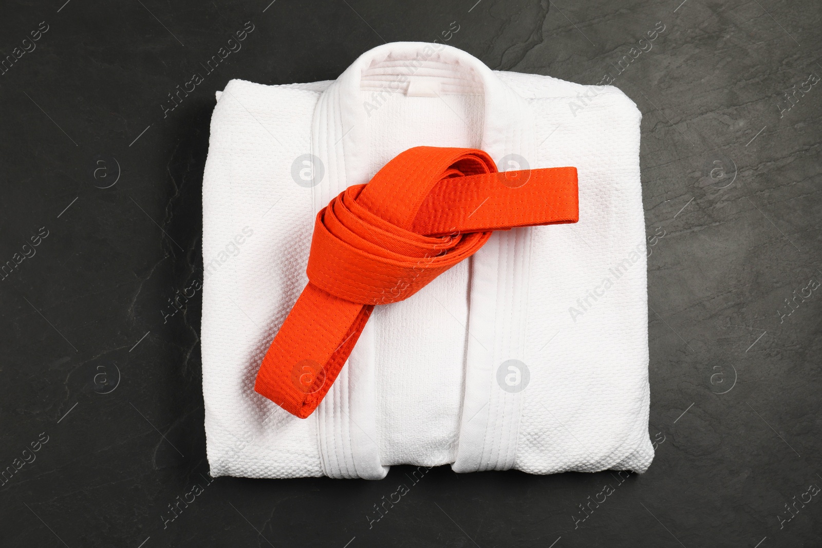 Photo of Orange karate belt and white kimono on gray background, top view