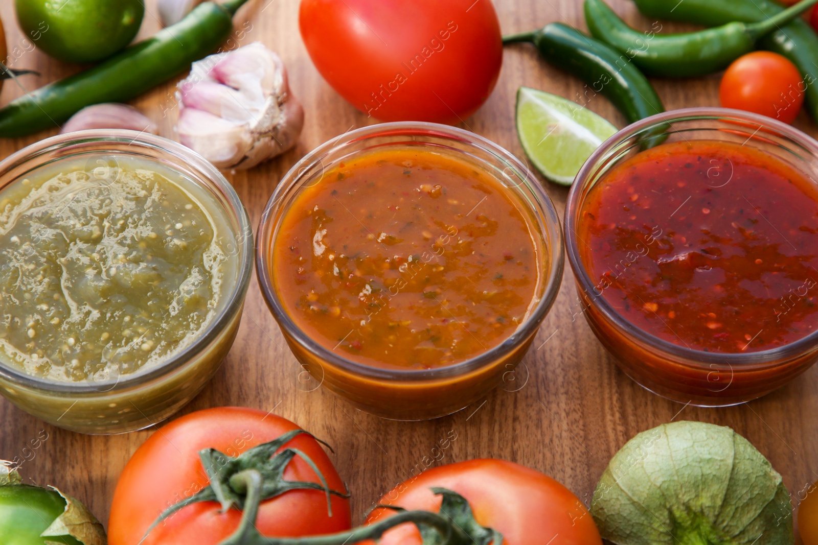 Photo of Tasty salsa sauces and ingredients on wooden table, above view