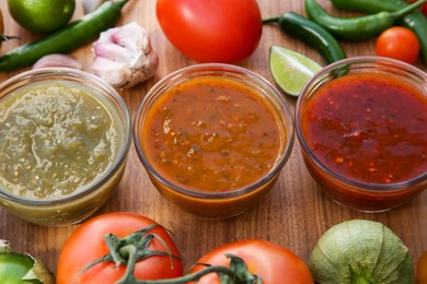 Tasty salsa sauces and ingredients on wooden table, above view