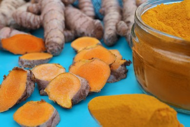 Photo of Glass jar of turmeric powder and roots on light blue tray, closeup